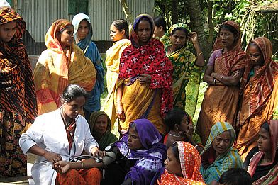 Inmitten einer Menschengruppe misst eine Ärztin den Blutdruck einer Patientin.