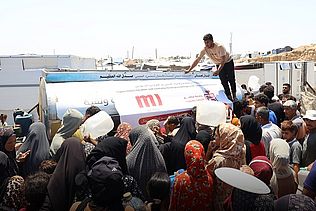Menschen mit Kanistern stehen vor einem Wassertransporter.