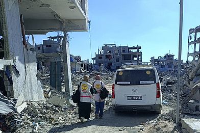 Mitarbeiter:innen der medico-Partnerorganisation PMRS laufen durch Trümmer in Gaza.