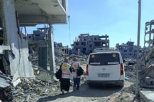 Mitarbeiter:innen der medico-Partnerorganisation PMRS laufen durch Trümmer in Gaza.
