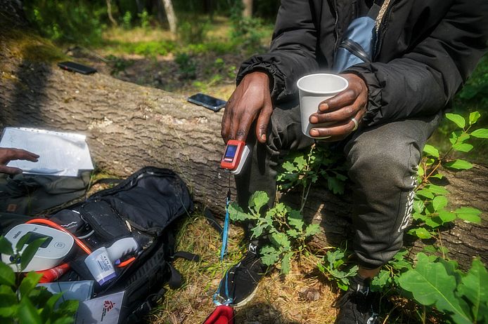 Ein Mensch mit einem Clip am Finger und einem Becher Tee in der Hand