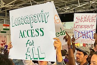 lenacapavir - Access for all" steht auf einem Schild, das ein Demonstrant bei einem Protest für die Freigabe des Patents auf das HIV-Prophylaxemedikament Lenacapavir hält.