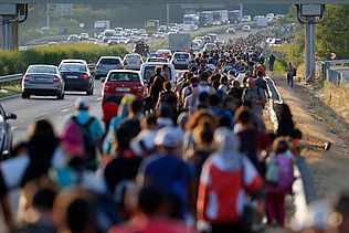 Eine große Menschengruppe läuft auf dem Standstreifen einer Autobahn.