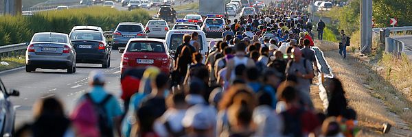 Eine große Menschengruppe läuft auf dem Standstreifen einer Autobahn.