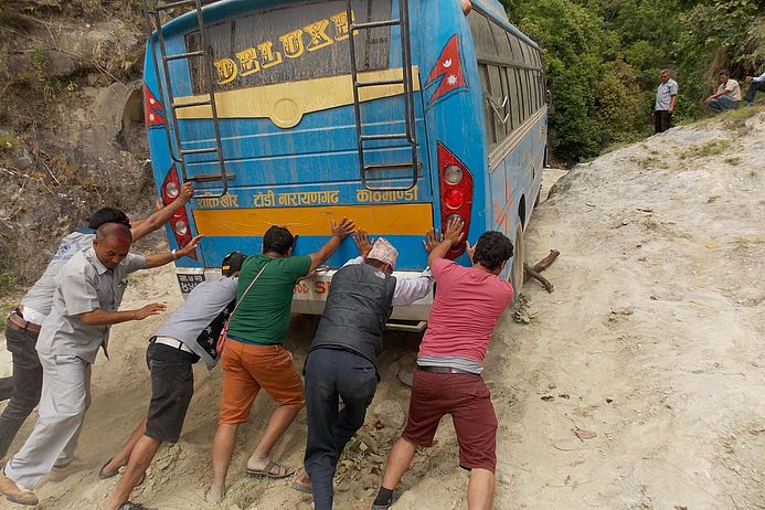 The picture shows people pushing a bus that is stuck in the mud.