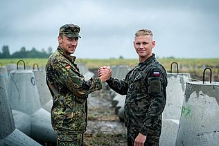 Ein deutscher und ein polnischer Soldaten stehen Hand in Hand an der polnisch-belarussischen Grenze.