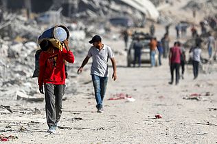 Ein Junge läuft bepackt durch Trümmer in Gaza.