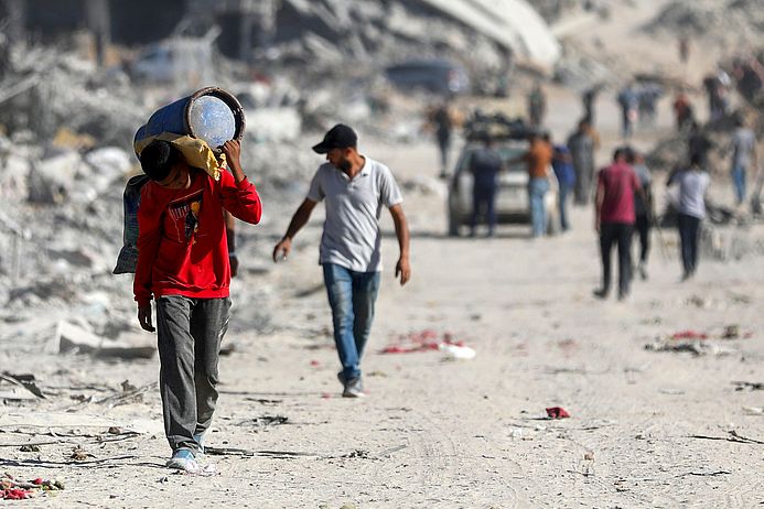 Ein Junge läuft bepackt durch Trümmer in Gaza.