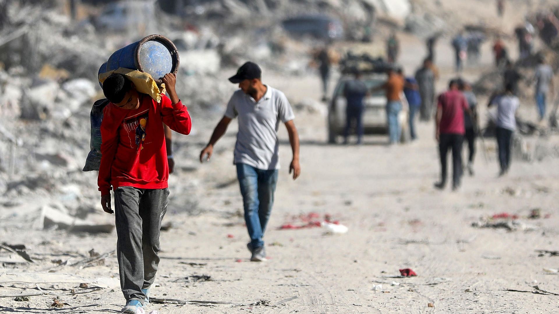 Ein Junge läuft bepackt durch Trümmer in Gaza.