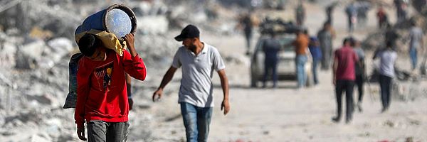 Ein Junge läuft bepackt durch Trümmer in Gaza.