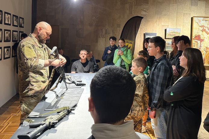 Kinder und Jugendliche stehen um einen Soldaten, der eine Waffe zusammenbaut.