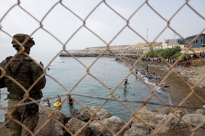 Ein Angehöriger des spanischen Militärs hält an einem Zaun Wache, während Menschen durch das Wasser waten und versuchen, nach Spanien zu gelangen. Ceuta, Spanien, 31.07.2026. REUTERS/Jon Nazca